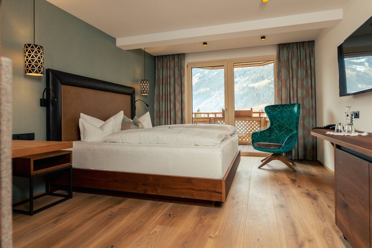 Een slaapkamer met een houten bed, een bureau, een stoel en een balkon met uitzicht op de bergen.