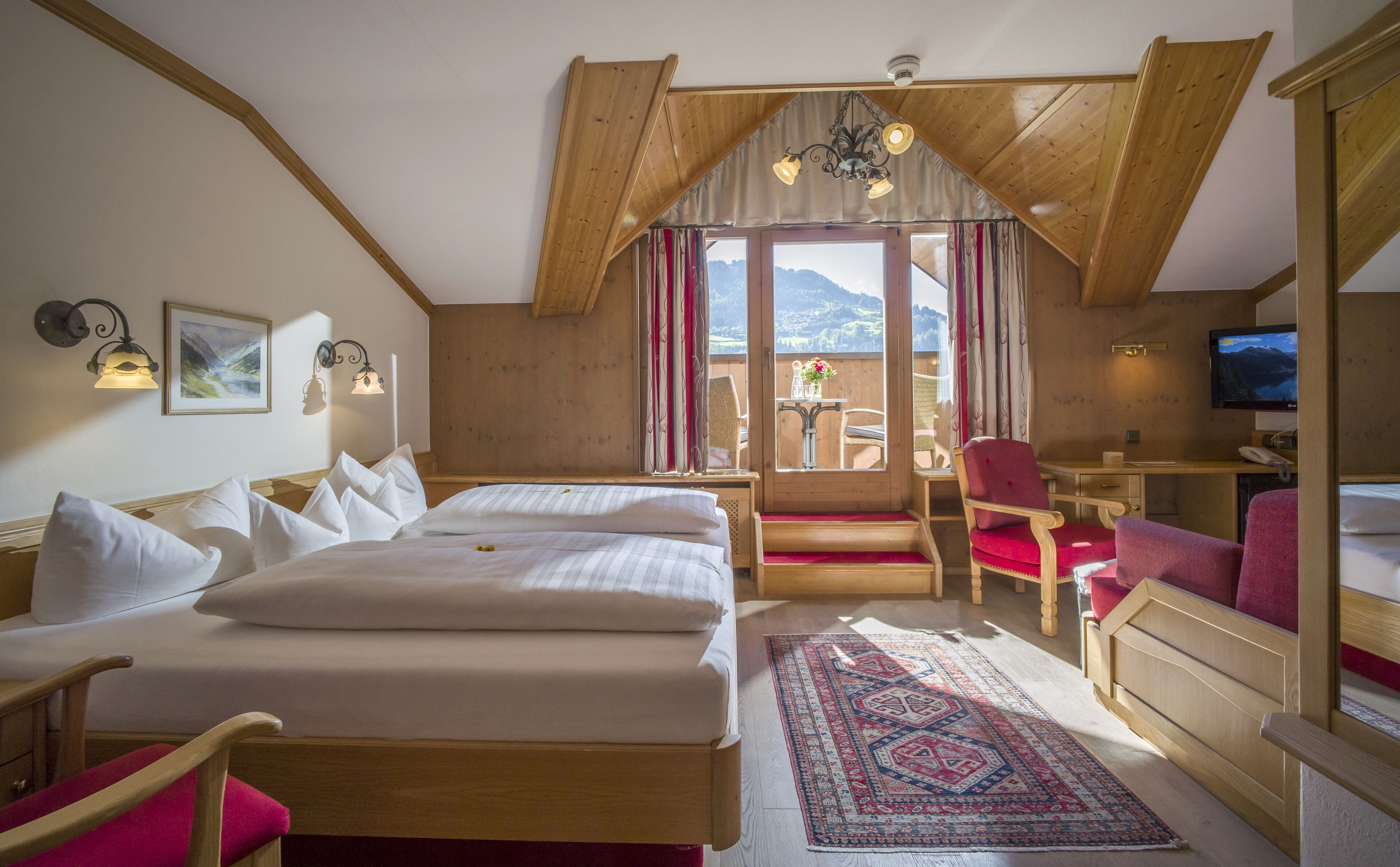 A hotel room with a large bed, a desk, a chair, a television, and a view of the mountains.