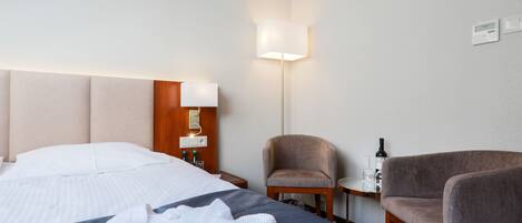A hotel room with a bed, a chair, a small table, and a lamp.