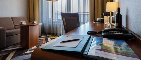 Habitación de hotel con sofá, escritorio con lámpara, teléfono y ventana con cortinas.