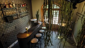 Een bar met een toonbank, krukken en planken vol flessen en glazen.