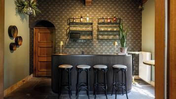 A bar area with a patterned wallpaper, a television, and multiple shelves with bottles. There are four stools in front of the bar.