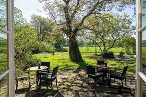 An outdoor patio with stone flooring and black wicker chairs, overlooking a grassy field and trees. - Landgoed Hotel & Restaurant Carelshaven (Delden)