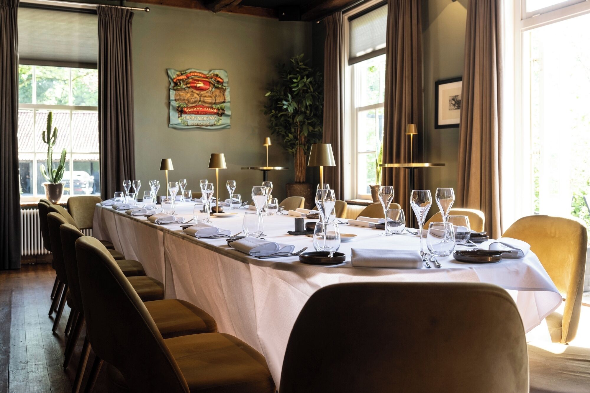 A long dining table set for a meal with chairs, lamps, and a cactus plant in the background.