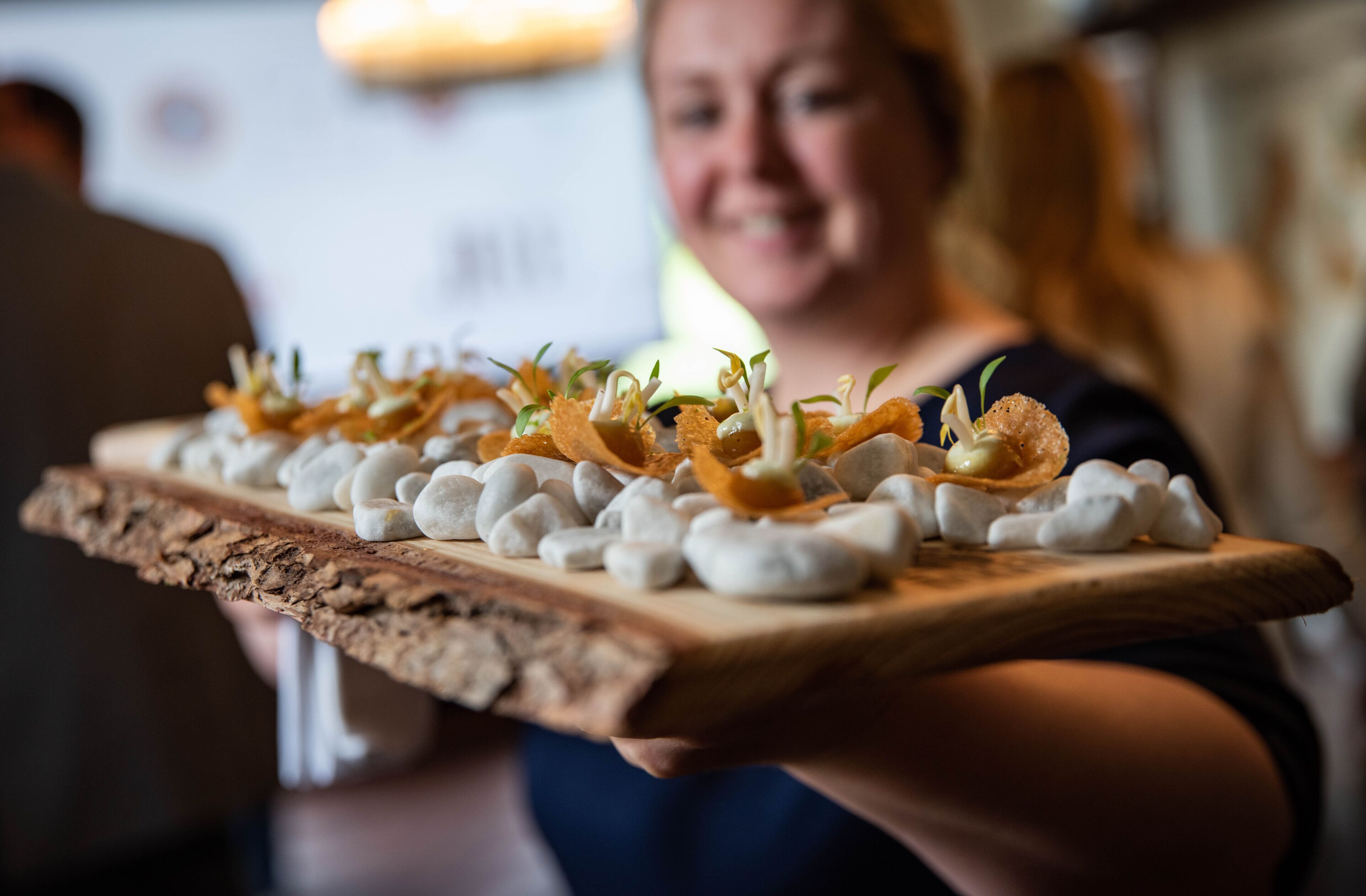 A wooden board with food items, including marshmallows and garnishes, being held by a person.