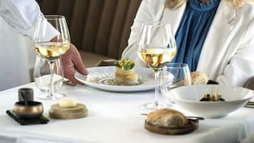 Une table à manger avec une assiette de nourriture, des verres à vin et un bol d’olives.