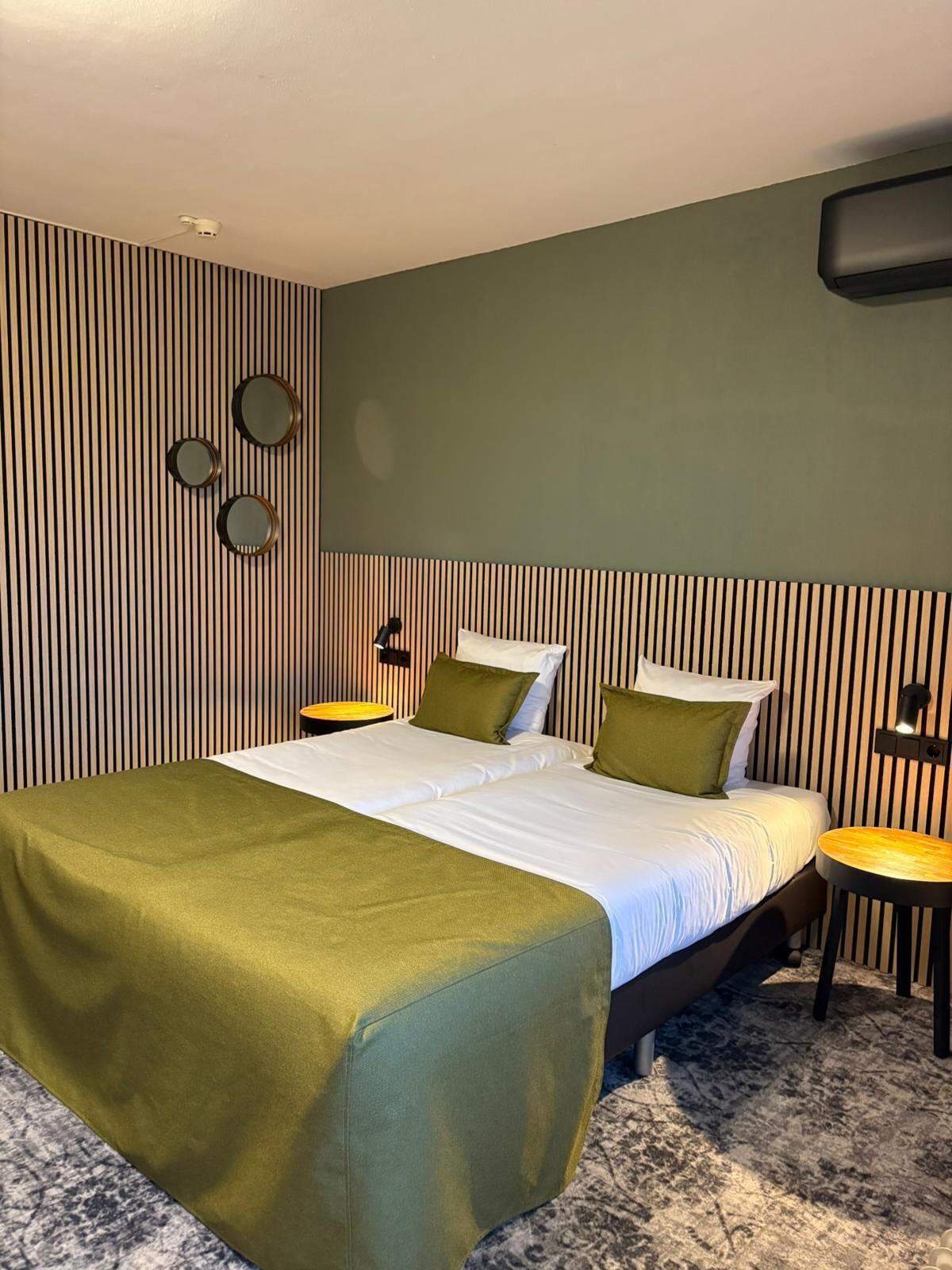 A hotel room with a large bed, two bedside tables, a wall-mounted TV, and a striped wall design.