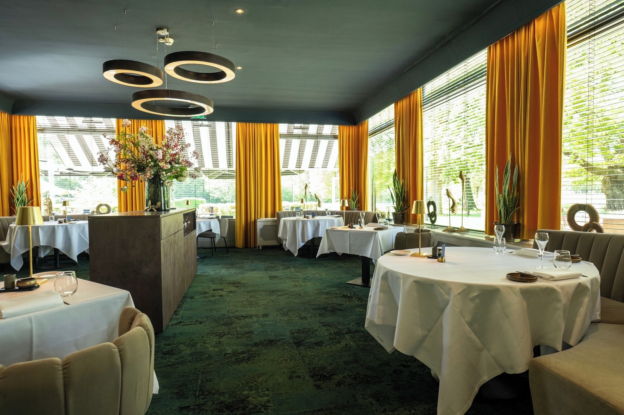 Un restaurante con mesas redondas, cortinas amarillas y una alfombra verde.