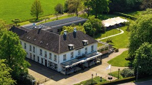 Een groot, wit gebouw met een pannendak, omringd door groene gazons en bomen.