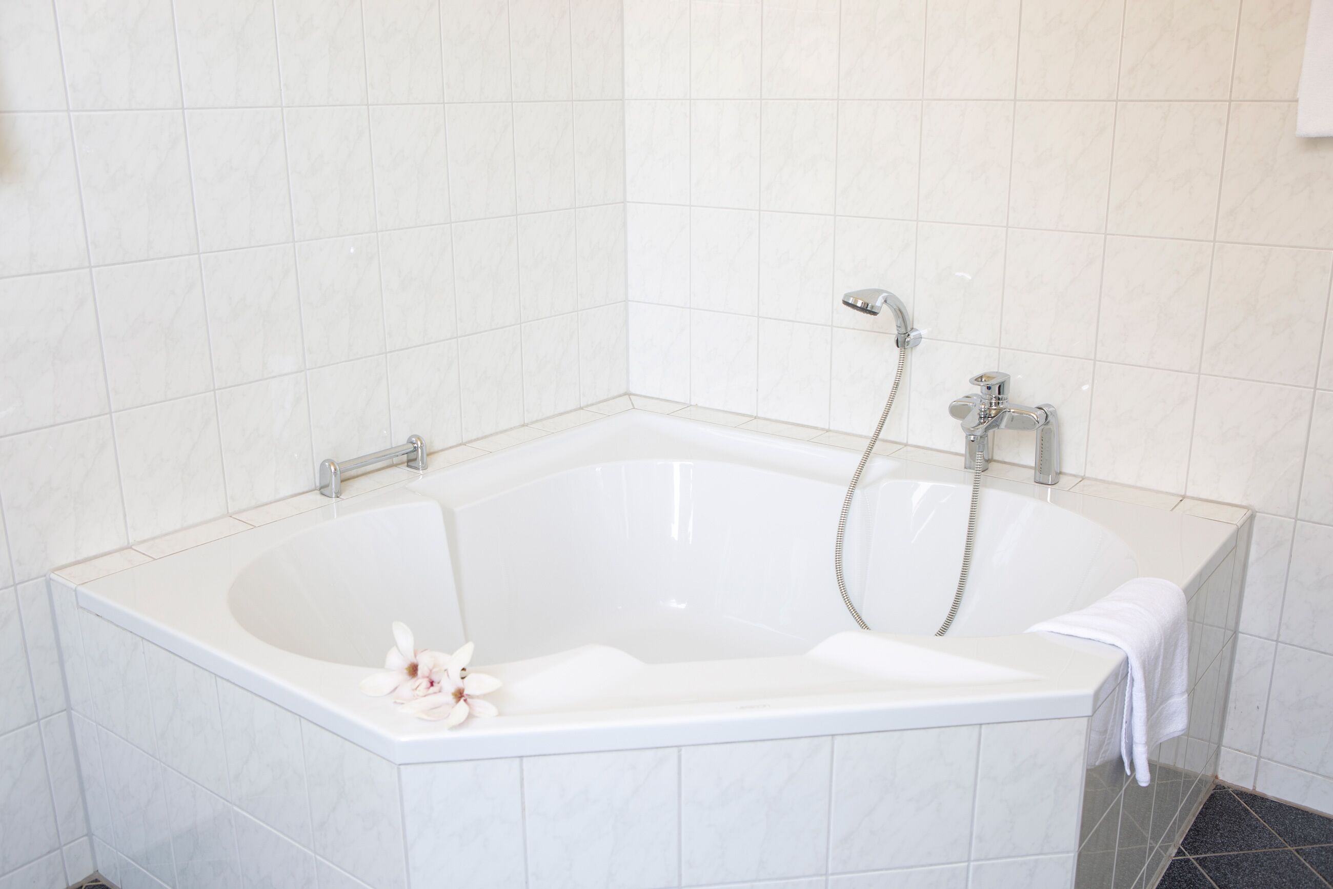 Una bañera blanca con ducha, una toalla y una flor.