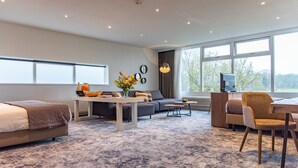 Een moderne hotelkamer met een groot bed, een zithoek, een eethoek en uitzicht op het omliggende landschap.
