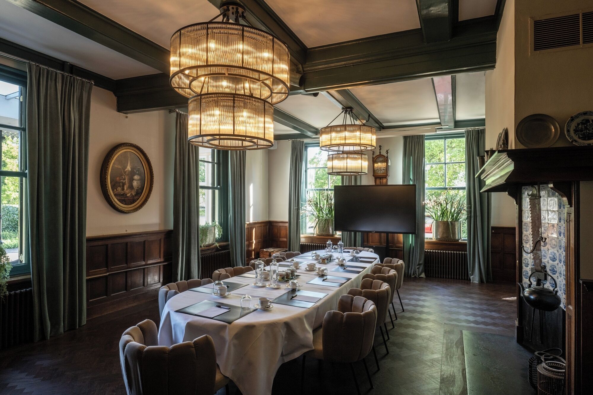 A dining room with a long table set for a meal, large chandeliers, and a fireplace.