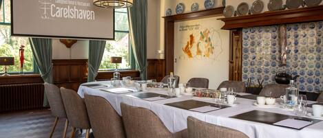 Un salón de conferencias en Landgoed Hotel & Restaurant Carelshaven con una pantalla de proyector, mesas de comedor, sillas y una pared decorativa con platos.