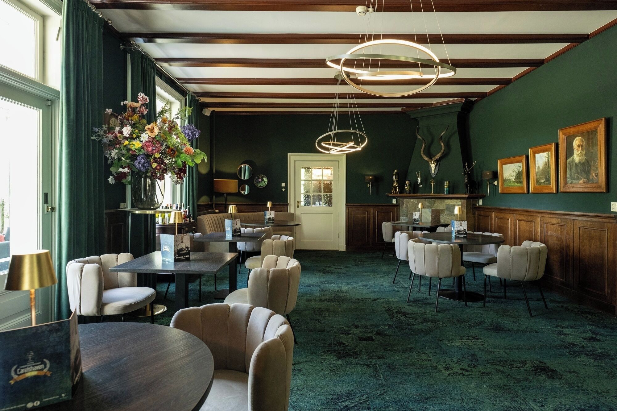 Vestíbulo de hotel con alfombra verde, vigas de techo de madera y un gran arreglo floral. Varias áreas de estar con mesas y sillas.
