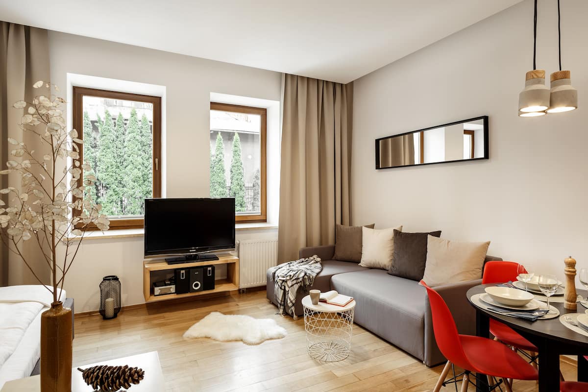 A modern living room with a flat-screen TV, a sofa, a dining table with red chairs, and a large window with curtains.