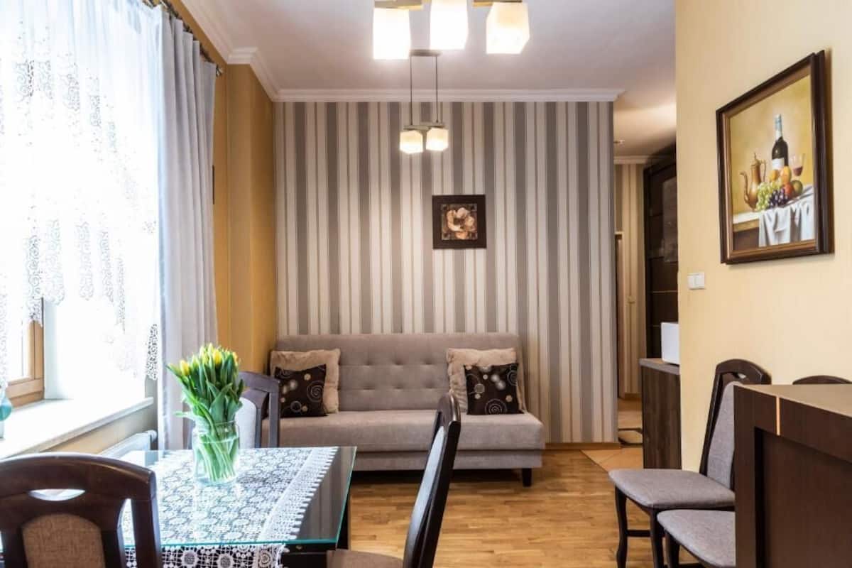 A dining area with a table, chairs, a sofa, a vase of flowers, a painting, and a striped wall.