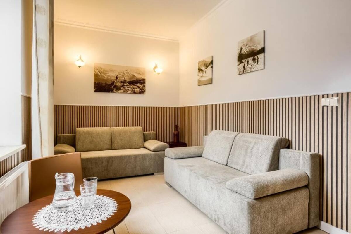 A living room with a sofa, a small table with glasses, and wall-mounted artwork.