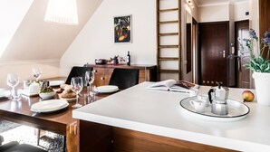 A dining area with a high ceiling, wooden beams, a white table, and a ladder against the wall. - Tatrytop Apartamenty Radowid (Zakopane)