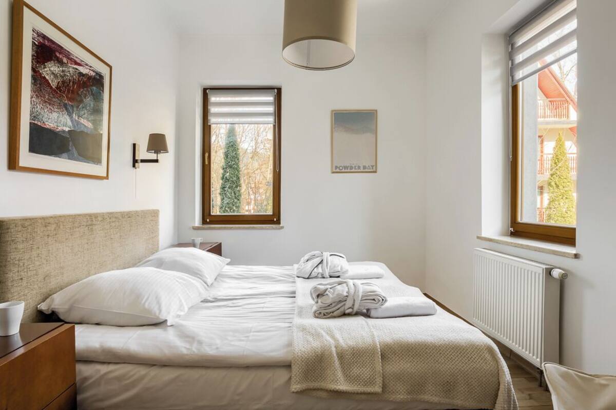 A hotel room with a bed, a window with a view, a framed picture on the wall, and a radiator.