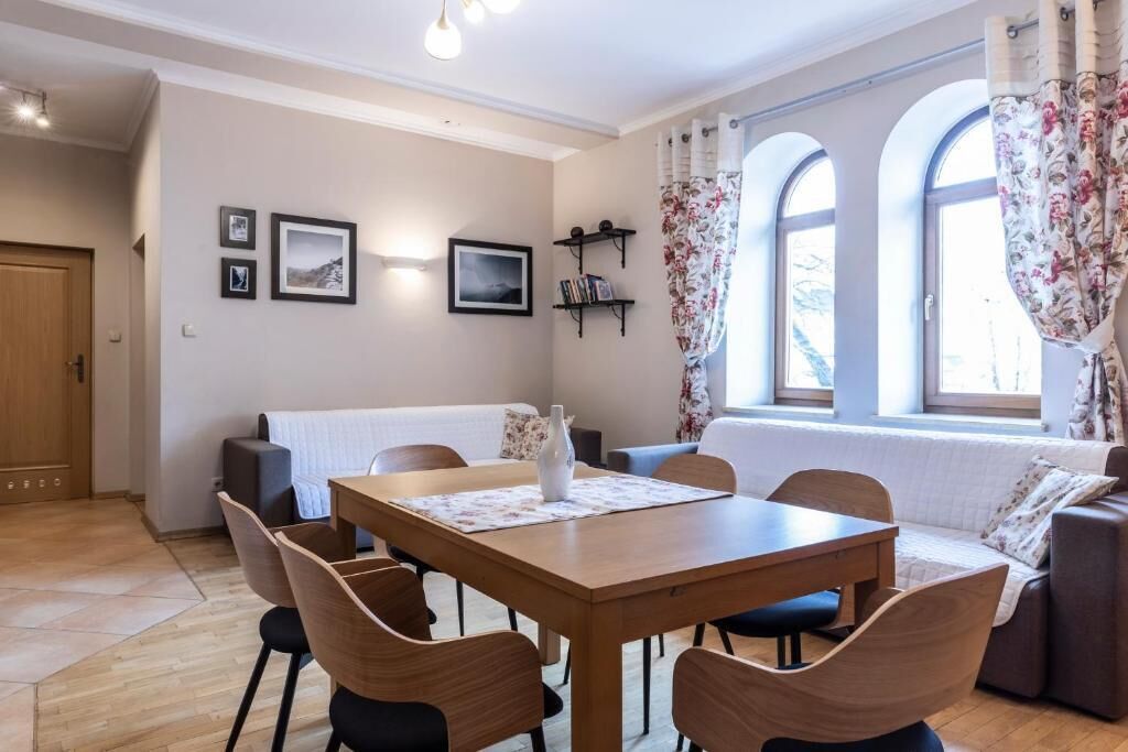 A dining area with a wooden table and chairs, a sofa, and a window with curtains.