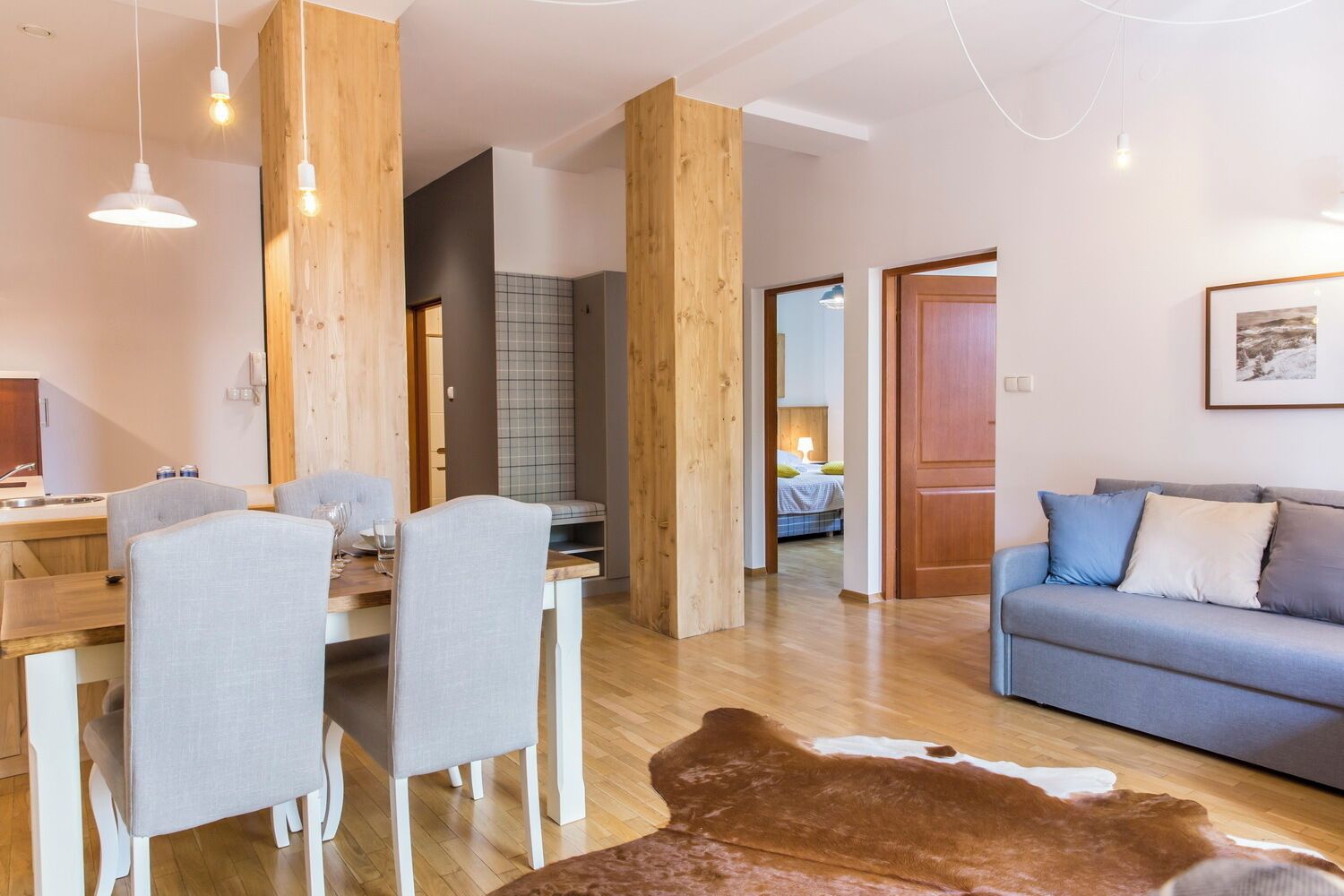 A modern living room with a dining area, wooden accents, a sofa, and a cowhide rug.