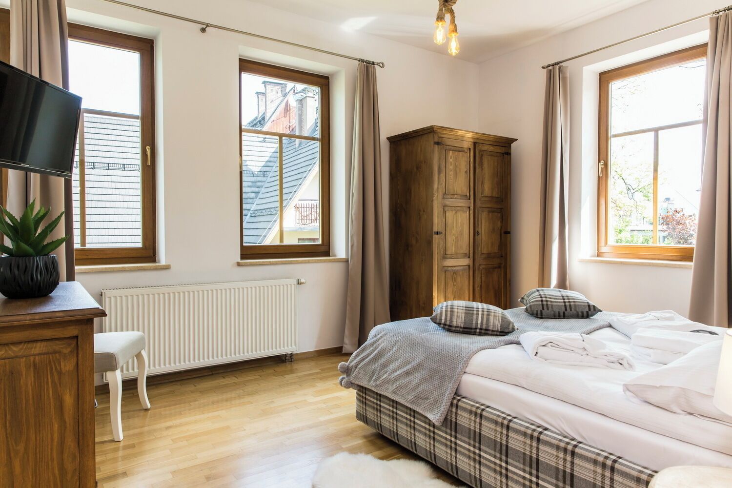 A bedroom with a bed, a wooden wardrobe, a radiator, a television, and a window with curtains.