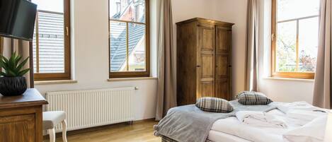 A bedroom with a bed, a wooden wardrobe, a radiator, a television, and a window with curtains.