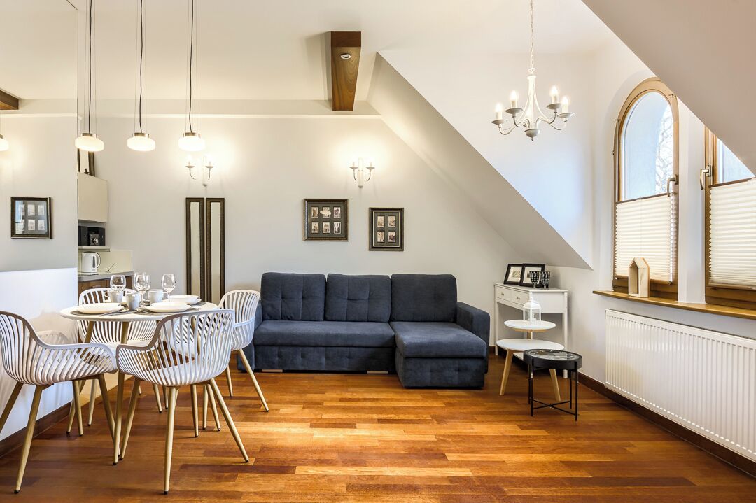 A modern living room with a dark blue sofa, white chairs, a dining table set, and a chandelier.