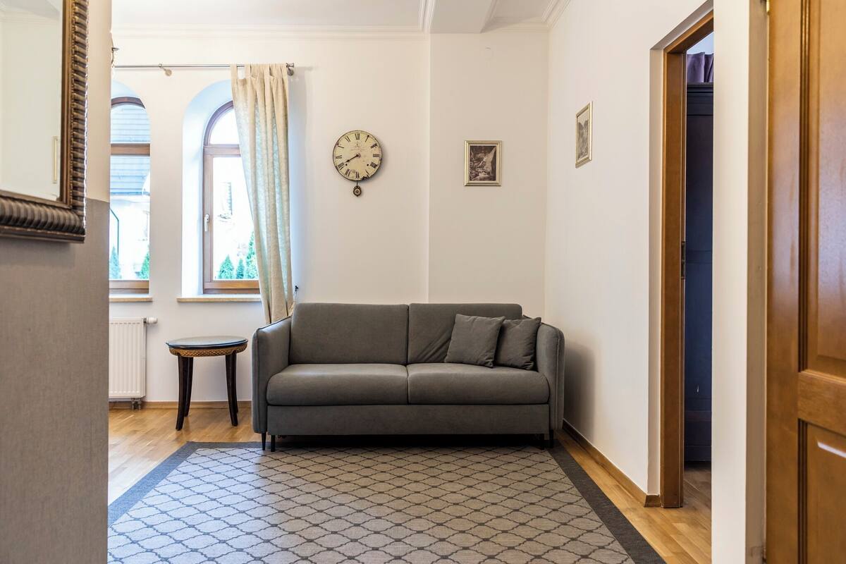 A living room with a sofa, a clock, a small table, and a patterned rug.