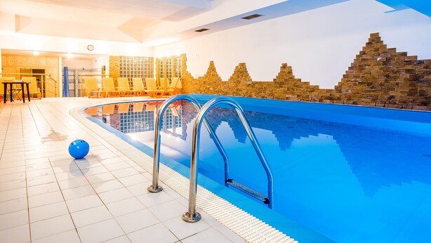 A swimming pool with clear blue water, a sunlit interior, and a brick wall with a geometric pattern. - Tatrytop Apartamenty Radowid (Zakopane)