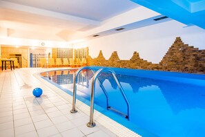 A swimming pool with clear blue water, a sunlit interior, and a brick wall with a geometric pattern. - Tatrytop Apartamenty Radowid (Zakopane)