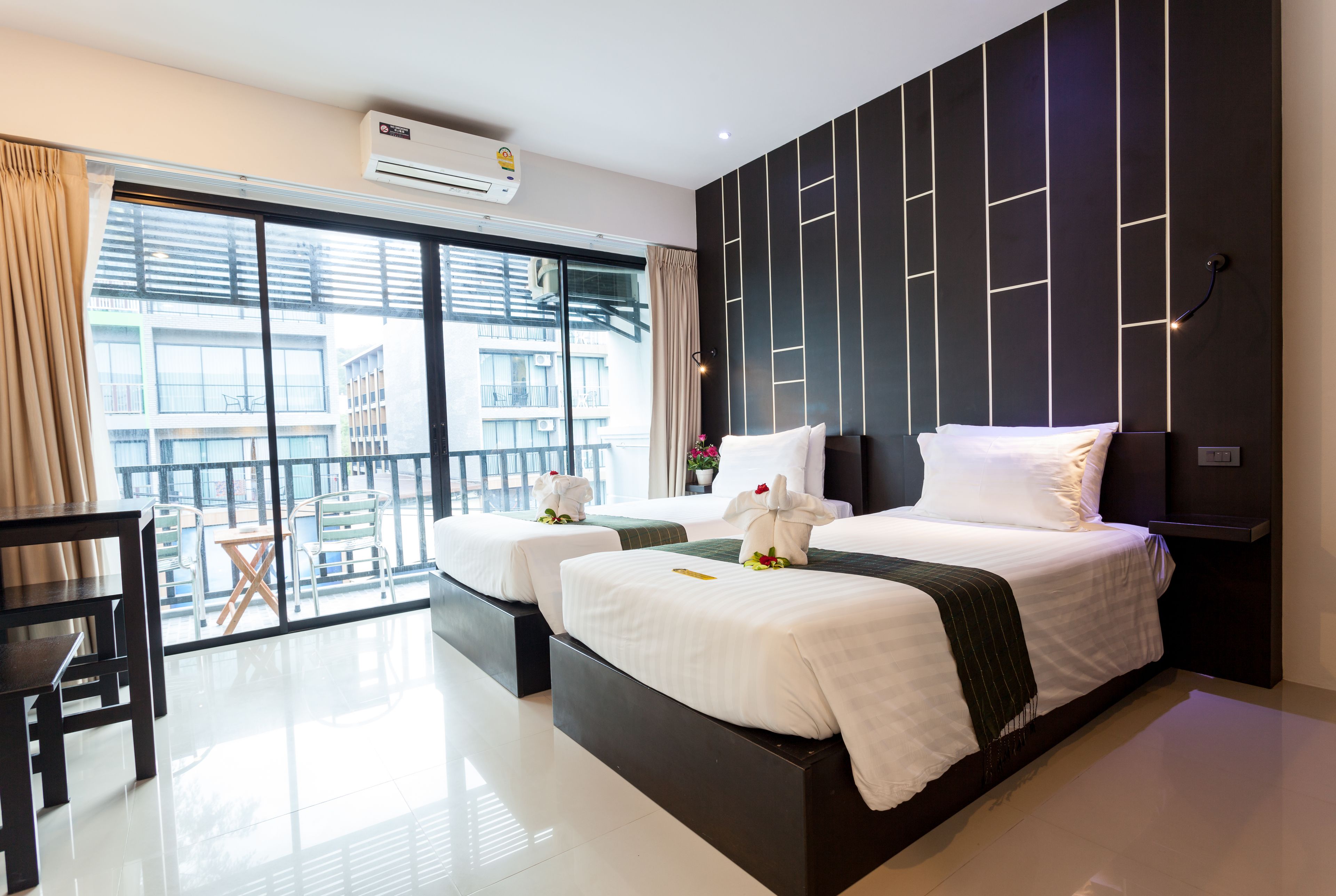 A modern hotel room with two beds, a balcony with a view of the city, and a large window with curtains.