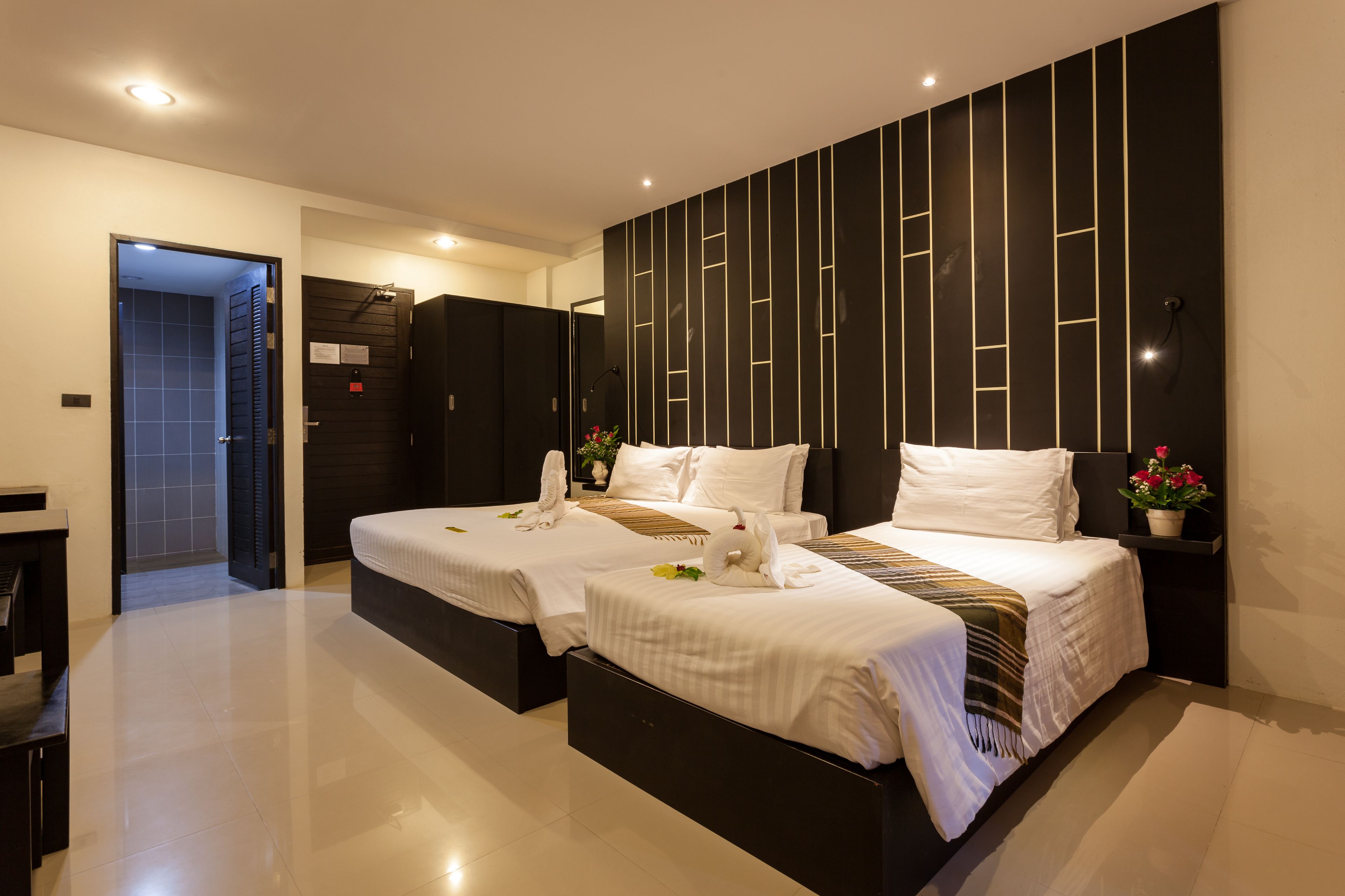 A modern hotel room with two beds, a dark accent wall, and a small potted plant.