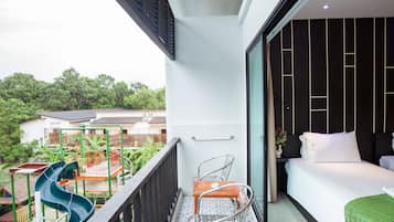 Un balcón con un tobogán, una cama con ropa blanca y vistas a zonas verdes y edificios.