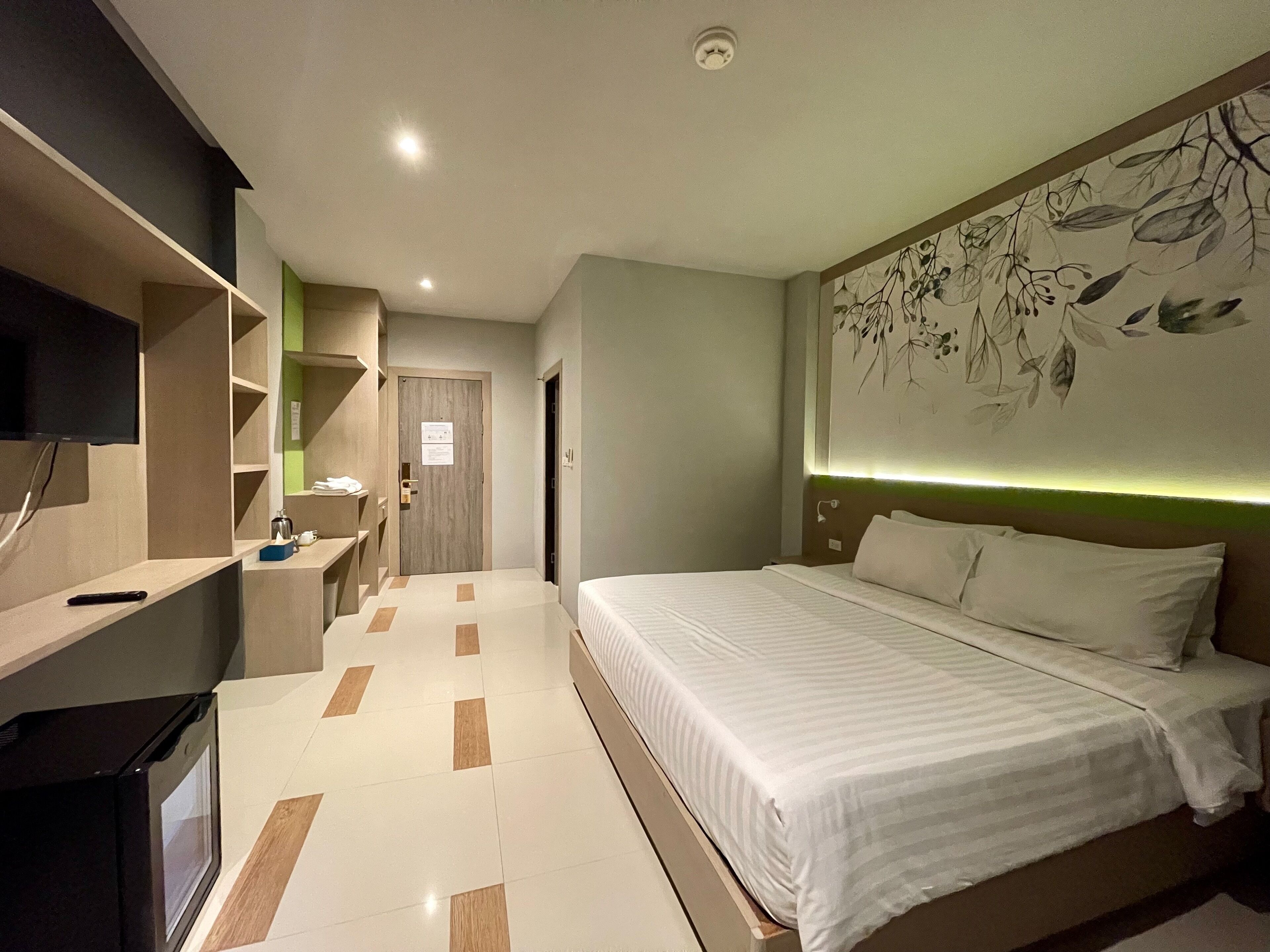 A modern hotel room with a large bed, a flat-screen TV, a desk with a chair, and a wall-mounted artwork.