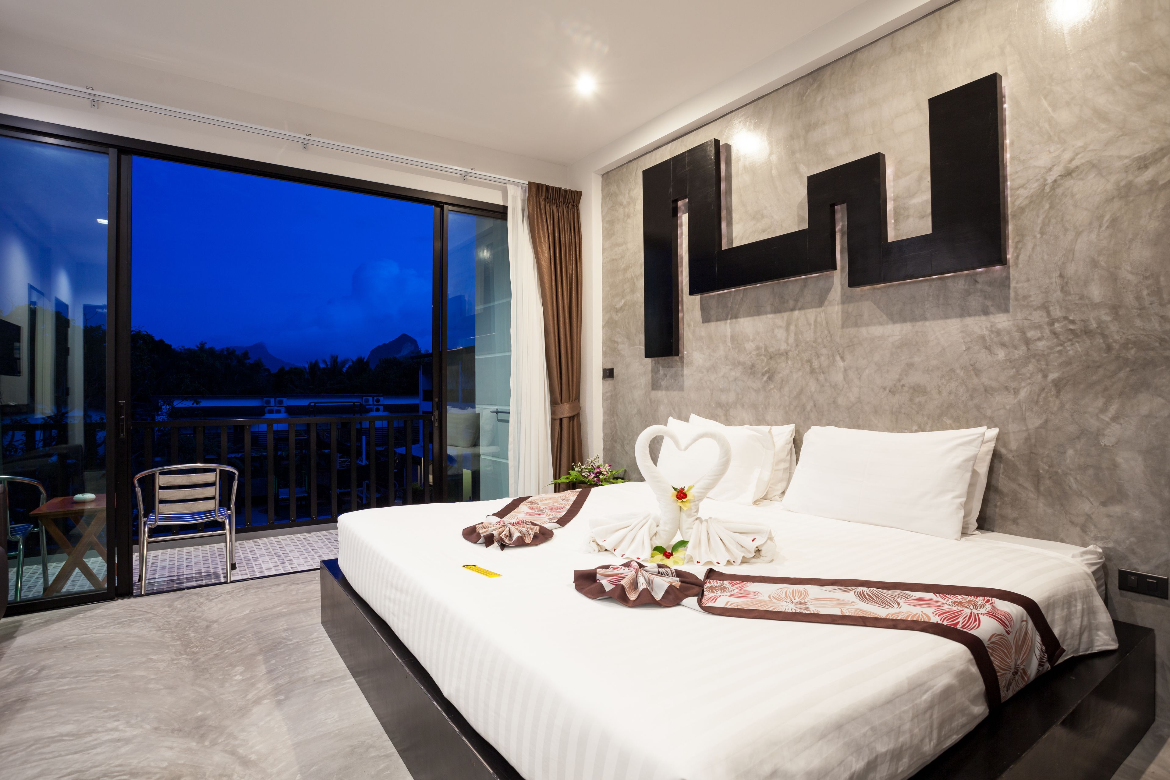 Una habitación de hotel moderna con una cama grande, vistas a las montañas a través de la ventana y un balcón con una silla.