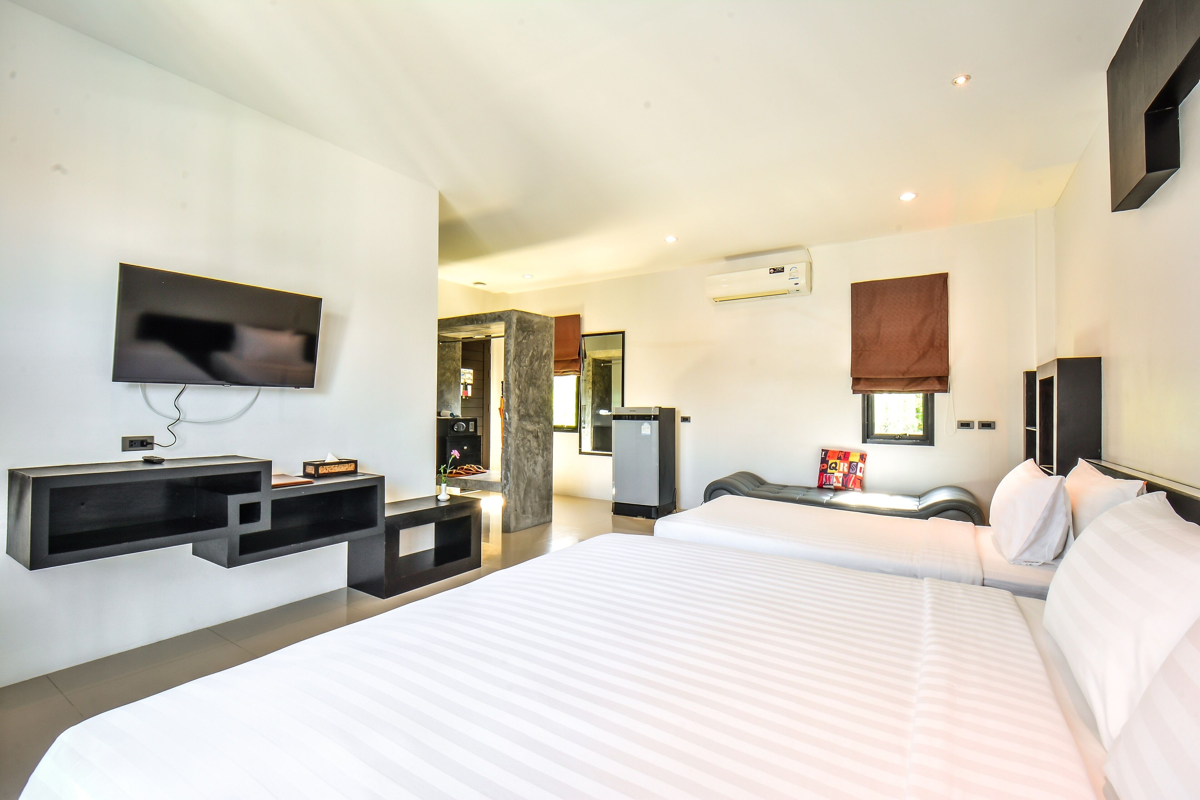 A modern hotel room with a large bed, a flat-screen TV mounted on the wall, a desk with a chair, and a small refrigerator.