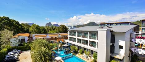 A hotel with a swimming pool, a children's play area, and a view of mountains.
