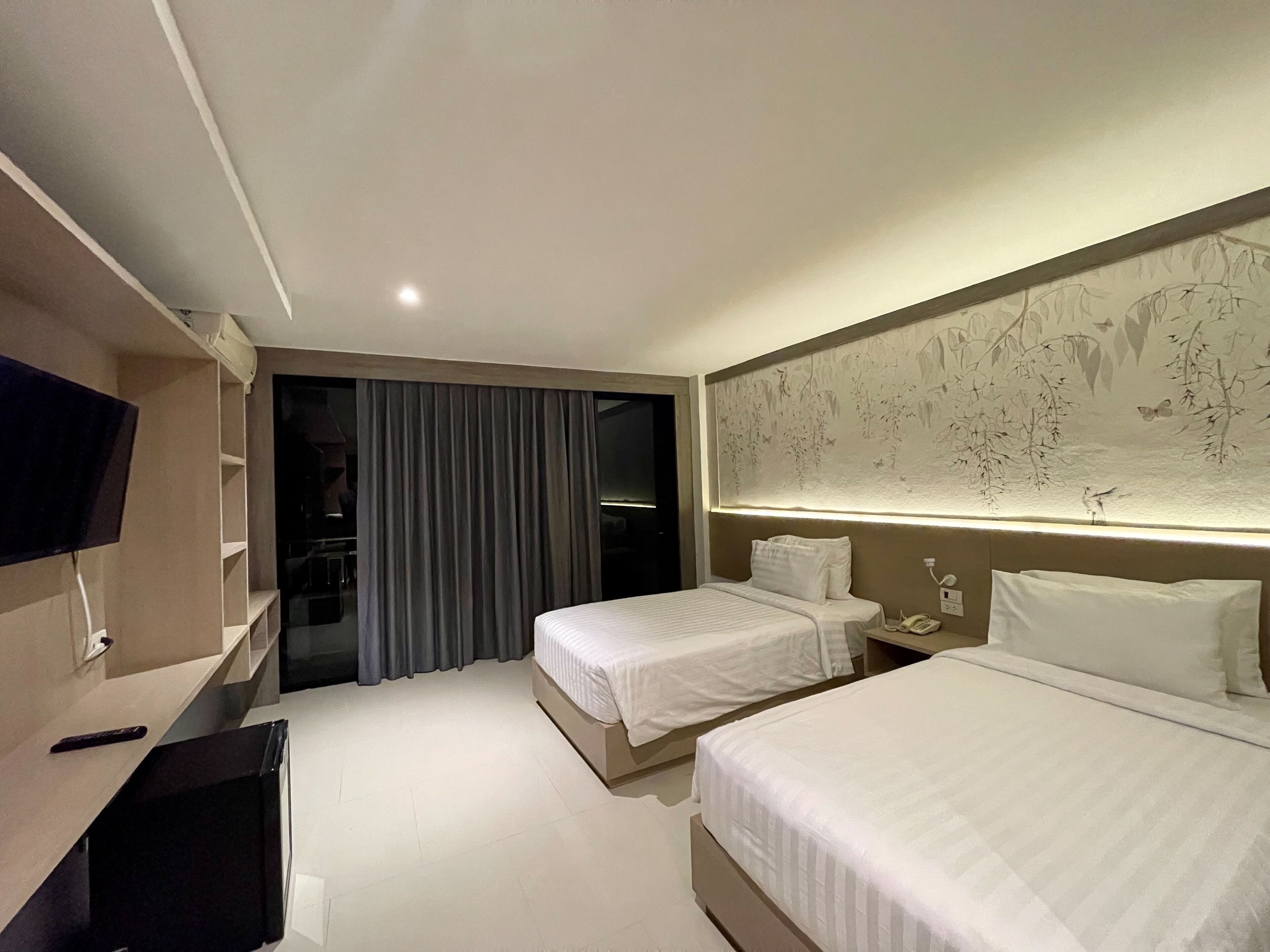 A hotel room with two beds, a TV, a desk, and a large mural on the wall.