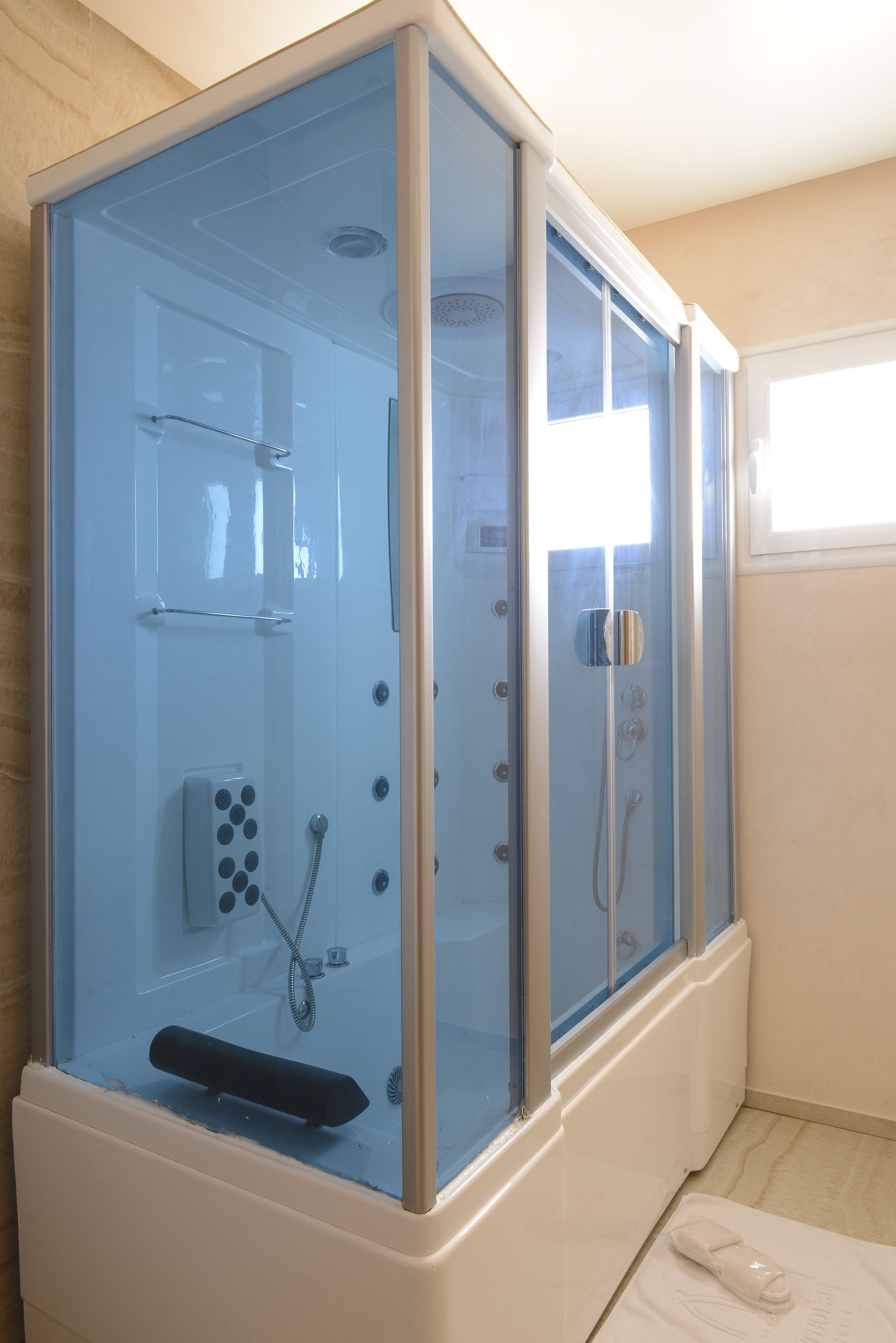 Un espace douche clos par des parois de verre, doté d’un panneau de commande, d’un pommeau de douche à main et d’un siège intégré.