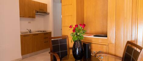 A dining area with a round glass table, wooden chairs, and a vase with red flowers.