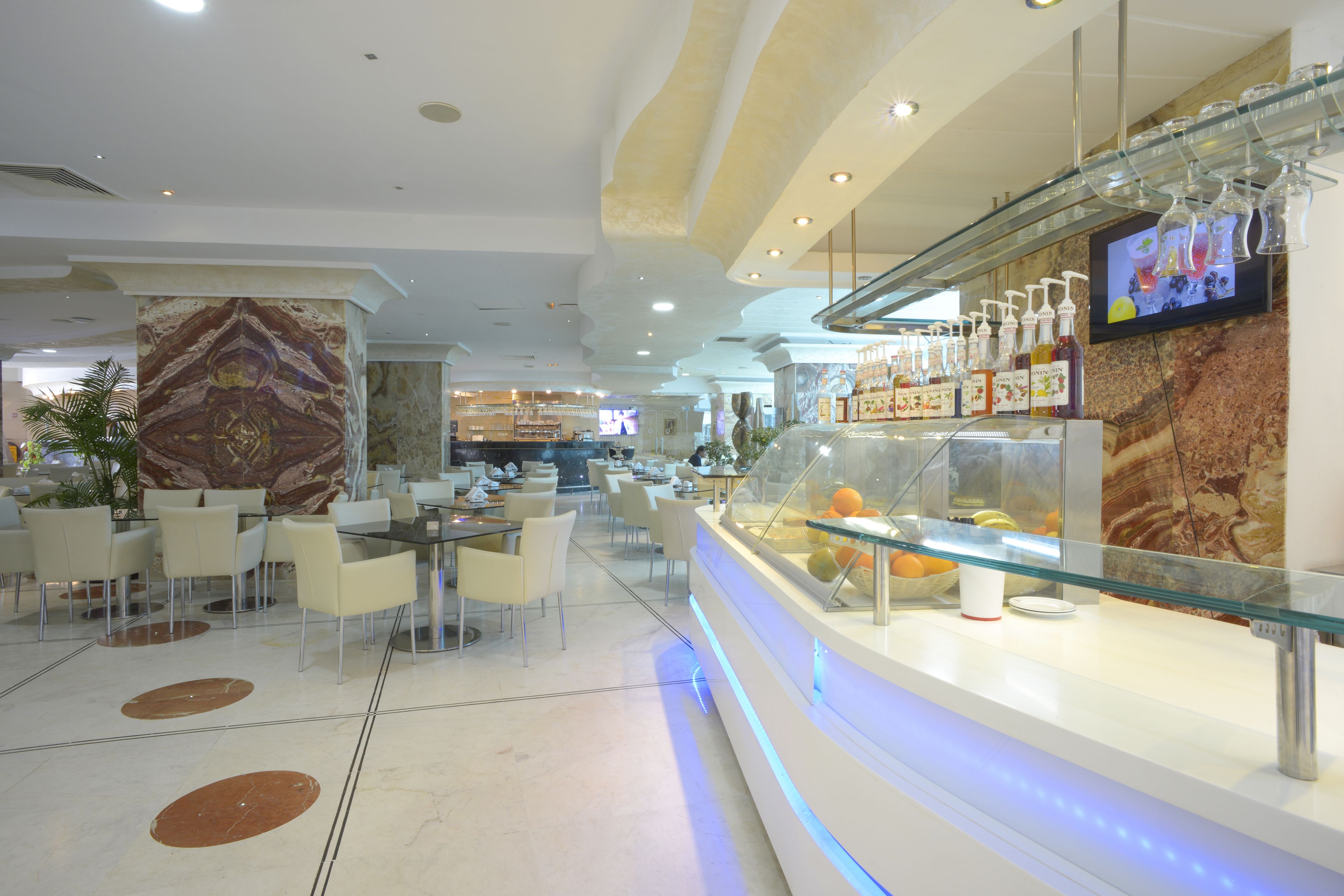 A modern restaurant with a marble column, glass display case with beverages, and a TV screen on the wall.