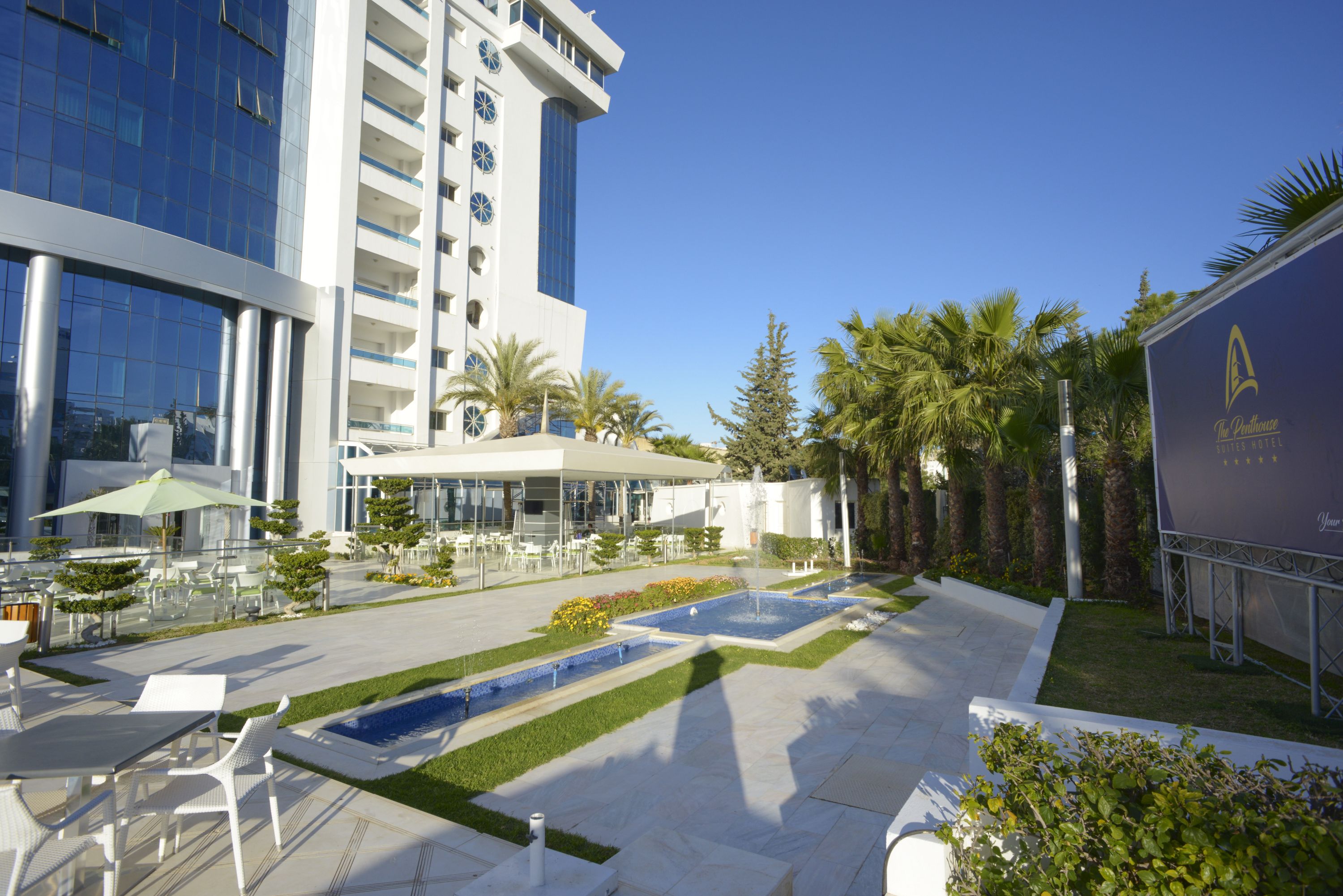 A modern hotel with a pool area, outdoor seating, and palm trees.