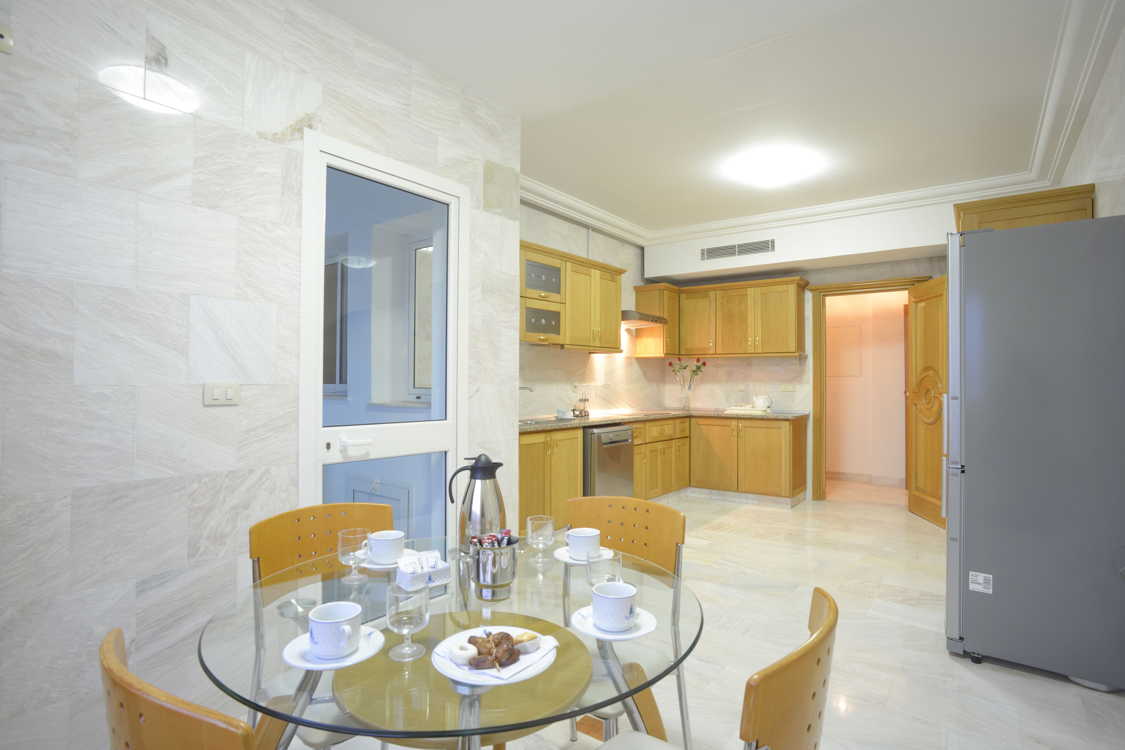 A modern kitchen with wooden cabinets, a glass dining table, and a refrigerator.