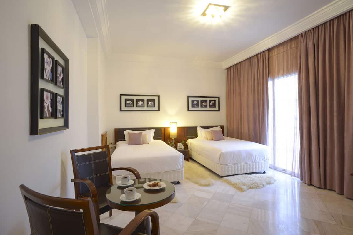 A hotel room with two beds, a dining table with chairs, and framed pictures on the wall.