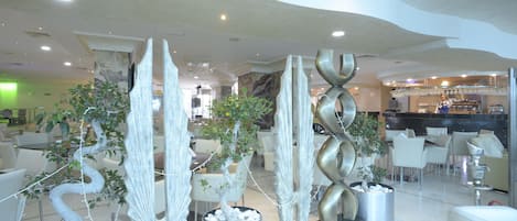 Un hall d’hôtel moderne, doté d’une décoration contemporaine, comprenant des sculptures abstraites et des plantes en pot.