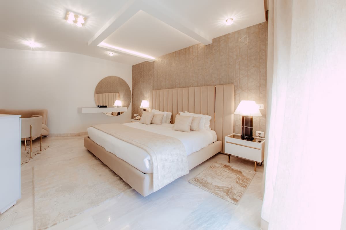 A modern bedroom with a large bed, bedside tables, a mirror, and a ceiling light fixture.