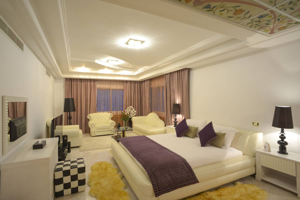 A hotel room with a large bed, two armchairs, a sofa, a small table, and a nightstand.