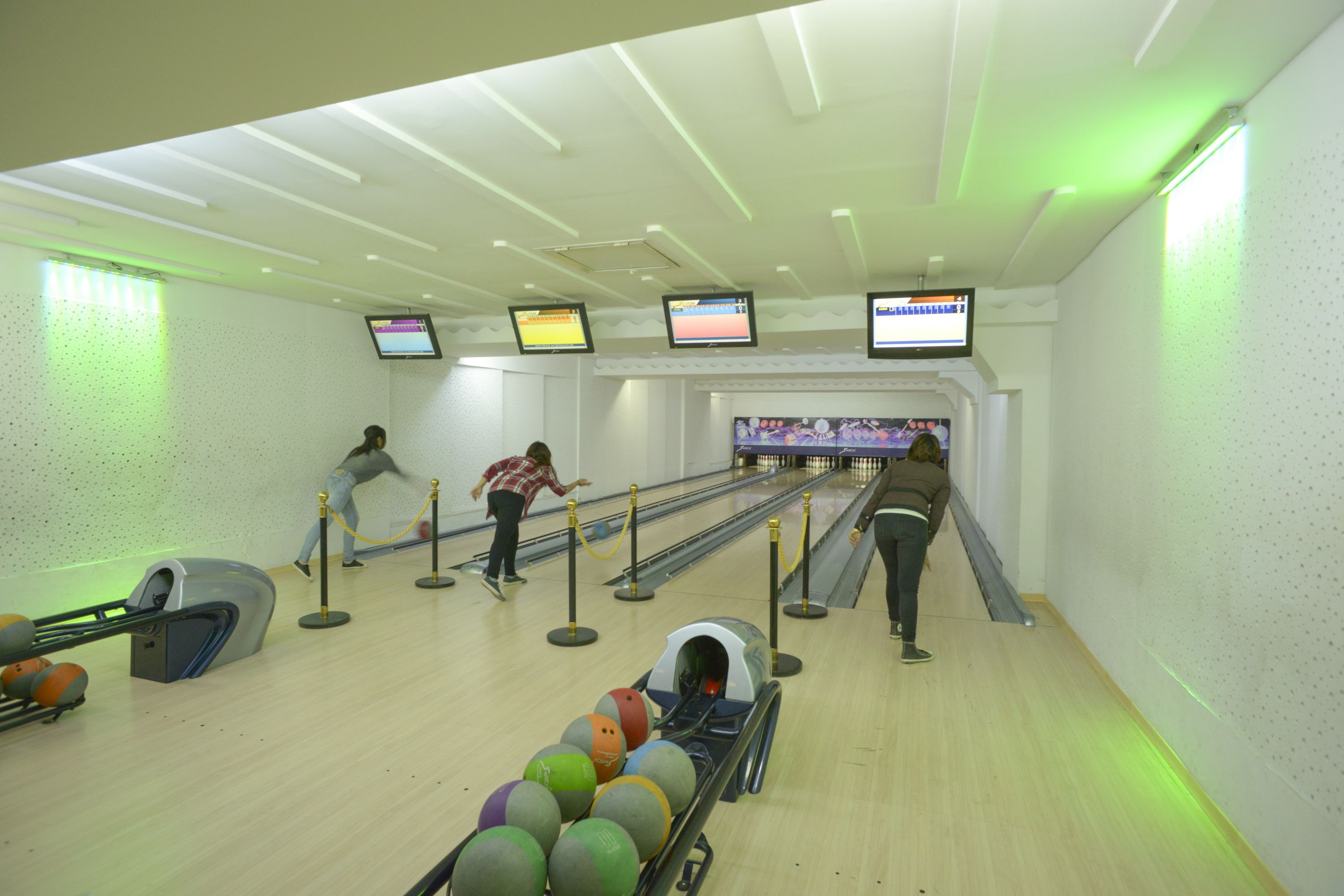 Une salle de bowling dotée de plusieurs pistes, d’un système de retour des boules et de trois écrans diffusant des parties de bowling.