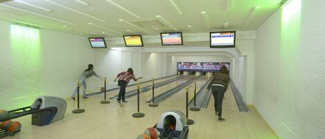 Una bolera con varias pistas, un devolutor de bolas y tres monitores mostrando juegos de bolos.